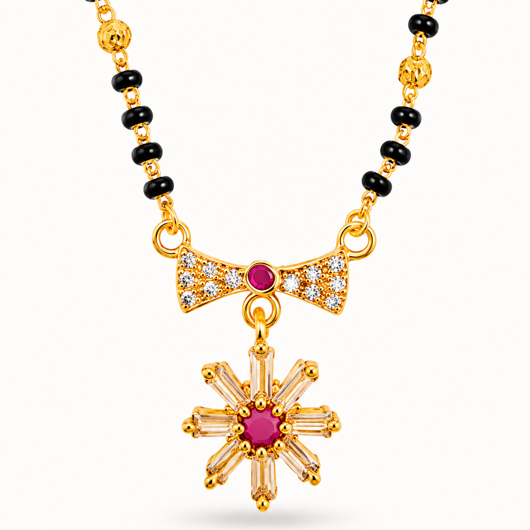 Gold-tone necklace featuring a beaded chain with alternating black and gold beads, a bow-shaped pendant set with small clear stones and a central pink gem, and a starburst pendant with a pink center and clear stones.